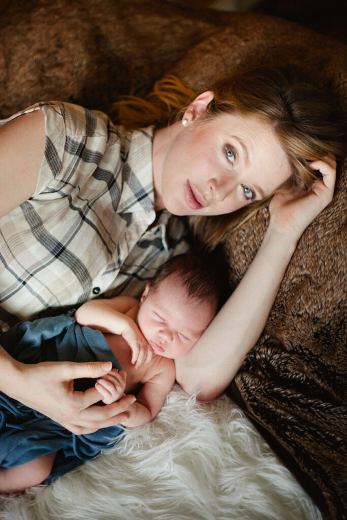 A mother and her newborn lay gently together, taking a much needed rest. The mother rests her head on one hand, while her other hand is draped over her child. He's holding one of her fingers, ever so gently in his sleep. She glances at us, proud and in awe of this young life.